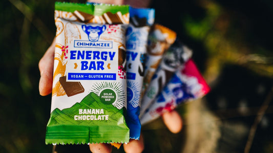 Hand holding a Chimpanzee Energy Bar Banana Chocolate, with more Chimpanzee Energy Bars fanned behind it